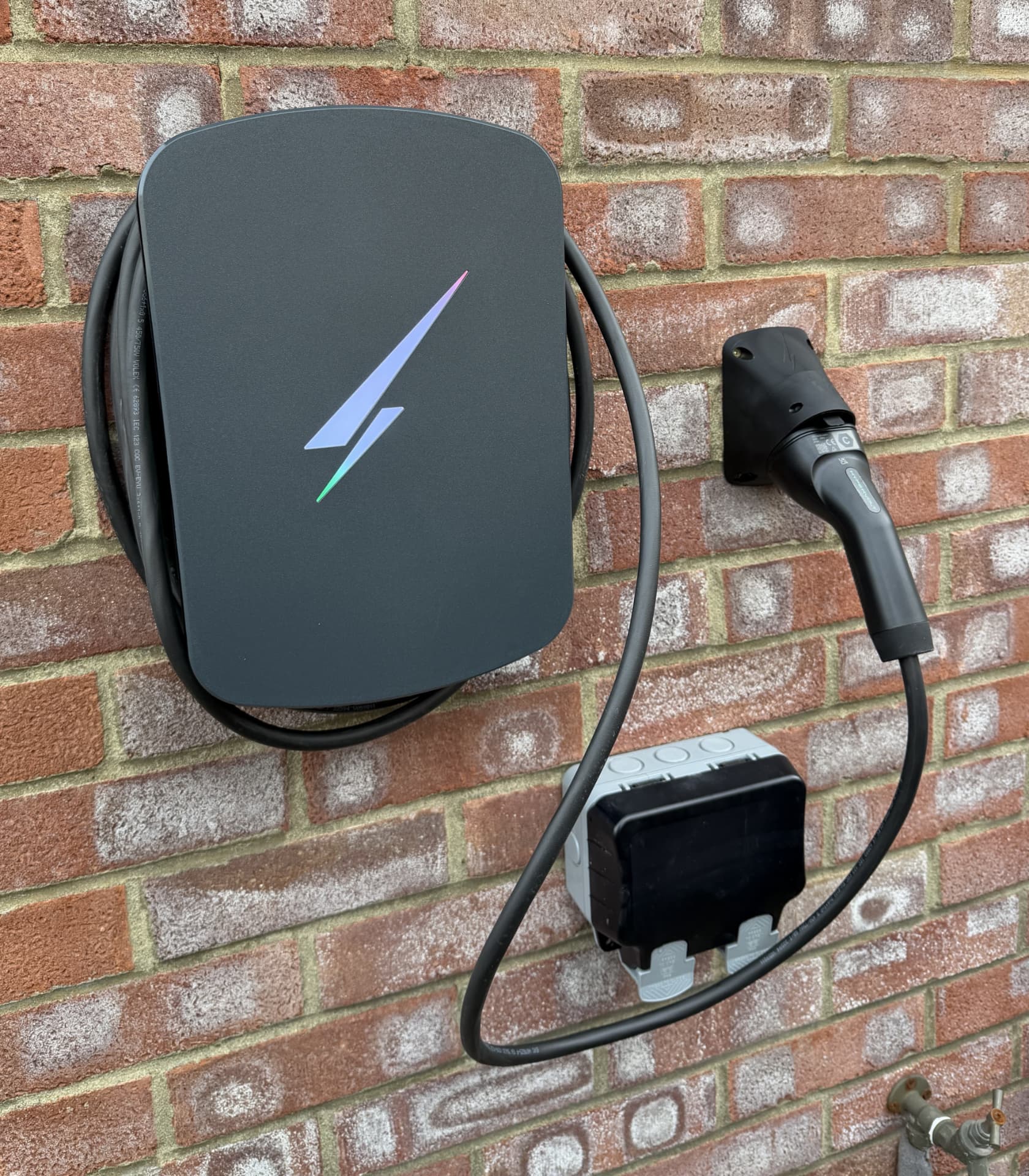 Wall-mounted EV charge point with coiled cable and weatherproof outdoor socket on a brick exterior wall