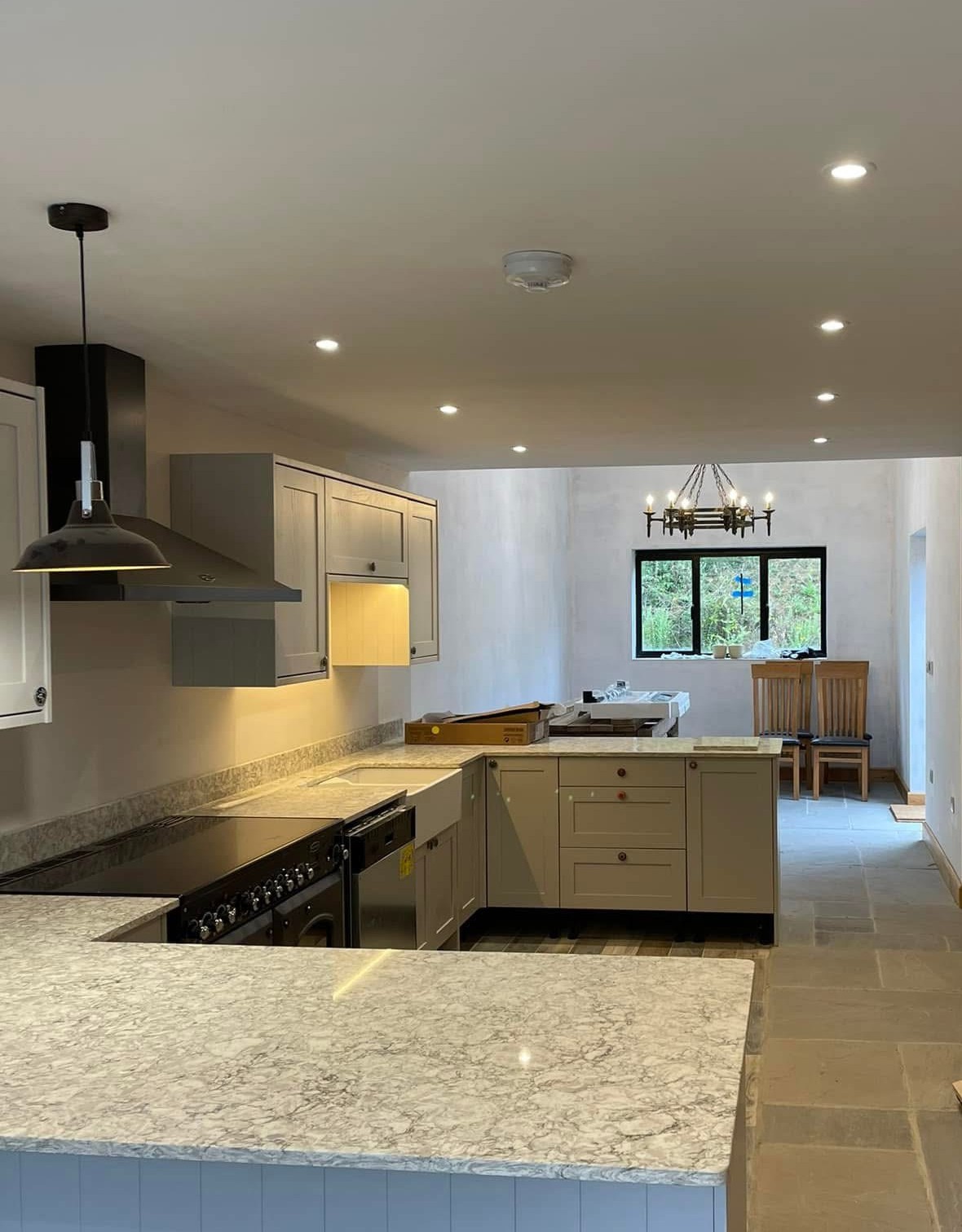 Kitchen renovation with veined quartz worktops, pale grey cabinets, a black range cooker and recessed downlights